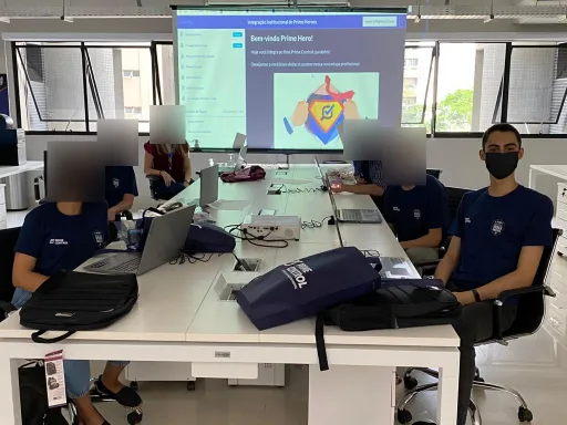 Integração dos novos funcionários na Prime Control em 15/10/2020: seis pessoas de máscara ao redor de uma mesa com notebooks, com Vittorio Perotto na ponta direita, de frente, e a projeção "Bem-vindo Prime Hero!". Os rostos das outras pessoas estão desfocados.